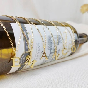 Creative display of gold initial letter necklaces draped on a wine bottle with fine chains