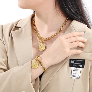 Detail view of gold coin pendant necklace and bracelet set worn on a model suit
