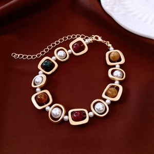 Détail d'un bracelet vintage doré avec pierres colorées et perles sur velours rouge
