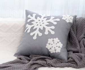 Detail of grey cushion cover with white snowflake embroidery on a cozy white sofa