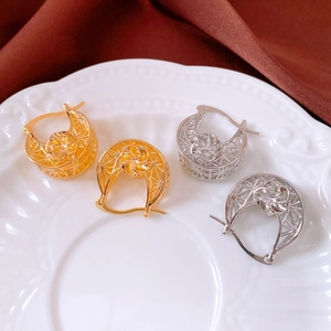 Detail view of 18K gold and silver hollow flower earrings on a ceramic display