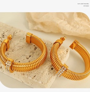 Detailed close-up of golden C-shaped twisted earrings with zircon stones on travertine