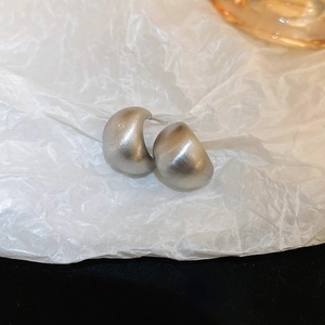 Detailed view of matte silver C-shaped earrings on textured white paper background