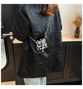 Back view of a mini black and white cow print chain crossbody bag on a black blazer