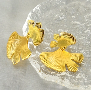 Detailed view of golden ginkgo leaf earrings with fine brushed metal texture on a tray