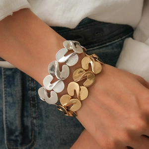 Detail of chunky gold and silver S-shaped twisted link bracelets on model's wrist