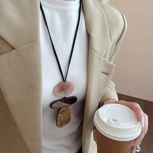 Detail of a resin geometric pendant necklace with black cord on a woman in beige blazer