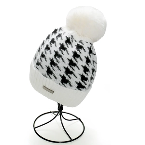 Dettaglio di un berretto da donna in maglia pied-de-poule con pompon bianco soffice