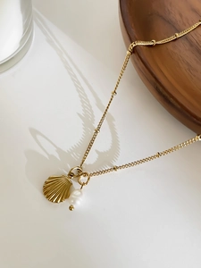 Detail of a gold seashell necklace featuring a white pearl pendant on a beaded chain