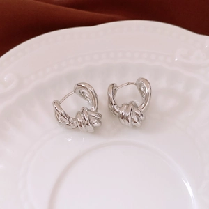 Macro shot of silver twisted knot earrings on a white ceramic plate with rich fabric