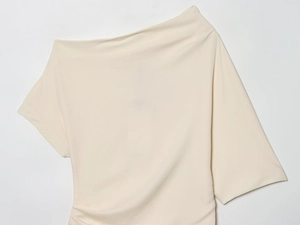 Detailaufnahme der cremeweißen asymmetrischen Bluse mit Webstruktur und Plisseefalten