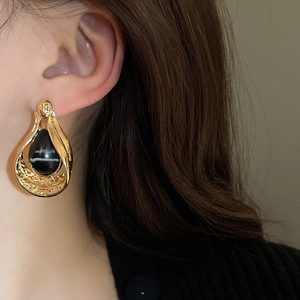 Close-up of model wearing vintage gold water-drop earrings with black stone inlay