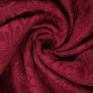 Dettaglio macro del pizzo rosso scuro con motivi floreali traforati e consistenza morbida