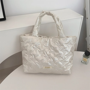 Detailed close-up of cream quilted tote bag with bow pattern and metal logo tag