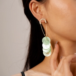 Detail of safety pin earrings with sparkling rhinestones and green mother-of-pearl discs