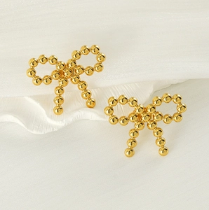 Close-up of golden bow-shaped stud earrings made of smooth metal beads on white fabric