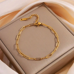 Detailed shot of golden paperclip chain bracelet with lobster clasp on silk fabric