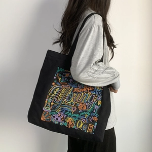 Detail view of black canvas tote bag with colorful Young embroidery worn by a model