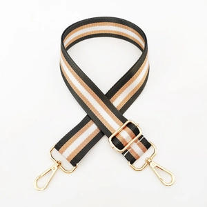 Detail of adjustable nylon bag strap with black, white, and brown stripes and gold buckles