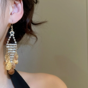 Detail of elegant gold tassel earrings with leaf-shaped metal scales and sparkling rhinestones