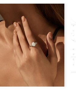 Elegant silver ring with oval opal stone and side diamonds shown on hand in warm natural light