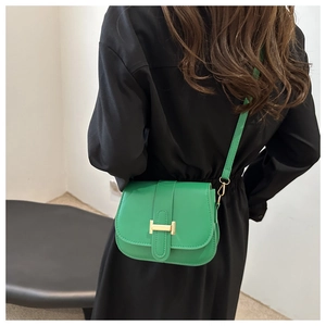 Detail view of bright green leather saddle bag featuring a bold golden H buckle on a model