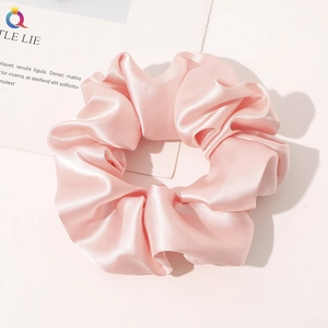 Macro detail of high-shine pink satin silk scrunchie with soft pleated texture