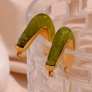 Detail of green acrylic earrings with gold metal frame hanging on a glass rim