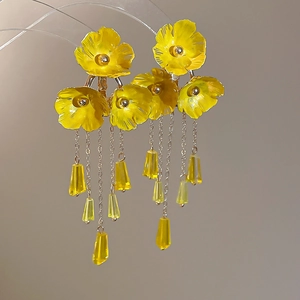 Makro-Detail von gelben Blumen-Ohrringen mit Kristallen am Acryl-Ständer