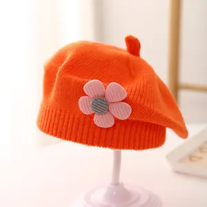 Detail of orange knitted beret showing pink floral decor and soft ribbed texture