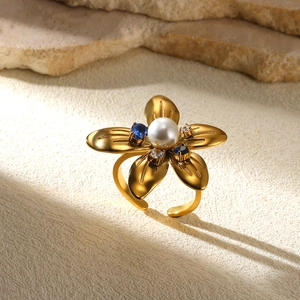 Exaggerated golden flower ring with central pearl and blue gemstones on stone surface