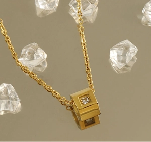 Close-up of golden square pendant with a clear crystal on a warm gold mirrored surface