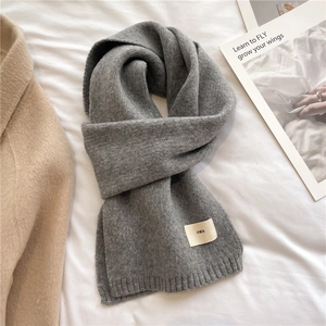 Detail of soft gray knitted scarf featuring a ribbed finish and a minimalist brand tag