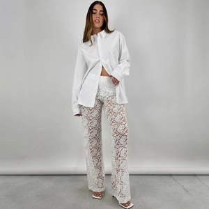 Dettaglio dei pantaloni a gamba larga in pizzo bianco a vita alta con motivi floreali