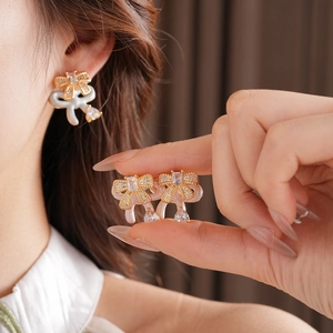 Detailed view of gold bow earrings with pink enamel, sparkling zircons and heart pendants