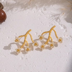 Detail of 18K gold-plated branch earrings featuring translucent white floral accents