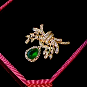 Detailed view of emerald teardrop brooch with gold leaf and bow zircon inlay