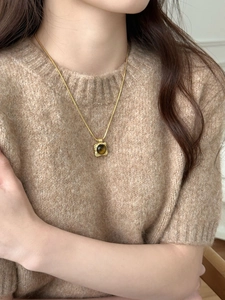 Golden square pendant necklace with brown tiger eye stone on a beige knit sweater