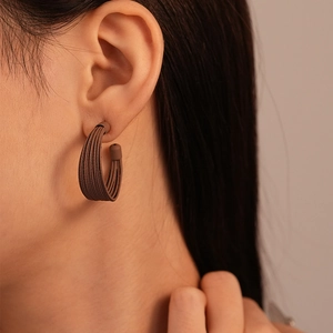 Close-up of minimalist C-shaped mocha brown earrings with matte brushed finish texture