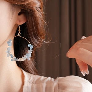 Detail of blue and white stone beads on gold circular drop earrings worn by a model