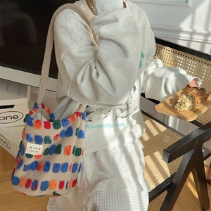 Detail of beige plush bucket bag with colorful pom-poms worn by model in casual outfit