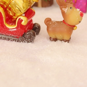 Miniature Christmas reindeer with red sleigh and gold gift boxes in artificial snow