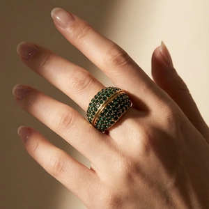 Close-up of a luxury 18k gold vintage ring with green pave crystals on a finger