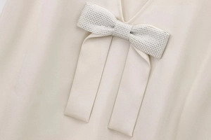 Detail of elegant beige dress featuring a V-neckline and a sparkling rhinestone bow