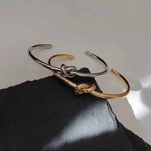 Polished gold and silver knot bangles displayed on a black textured stone background