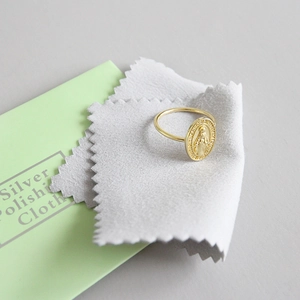 Gold Virgin Mary relief ring displayed with grey silver polishing cloth and instruction card
