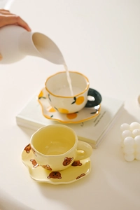 Close-up of hand pouring milk into a cute ceramic lemon patterned coffee cup with saucer