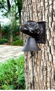 Detailed view of an antique cast iron dog head door bell mounted on a rustic tree trunk