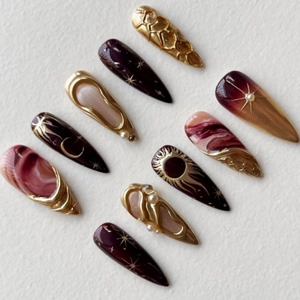 Detail of luxury stiletto press-on nails with burgundy, pearls, and gold celestial 3D art