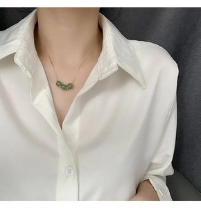 Detail of three green jade beads on a thin gold titanium necklace worn by a model